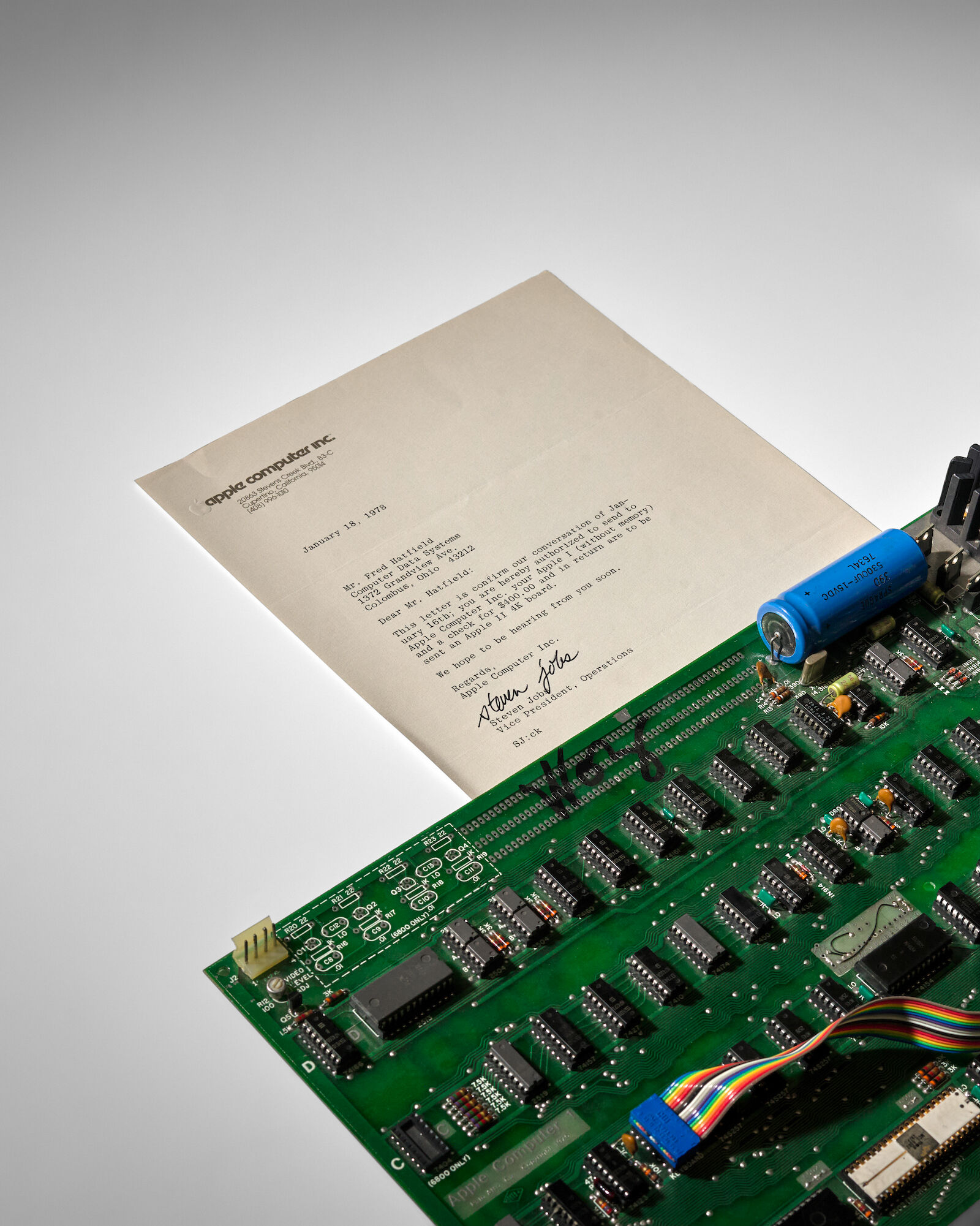 La lettre dactylographiée de Steve Jobs posée sur la carte mère verte de l'Apple-1, sur fond gris.