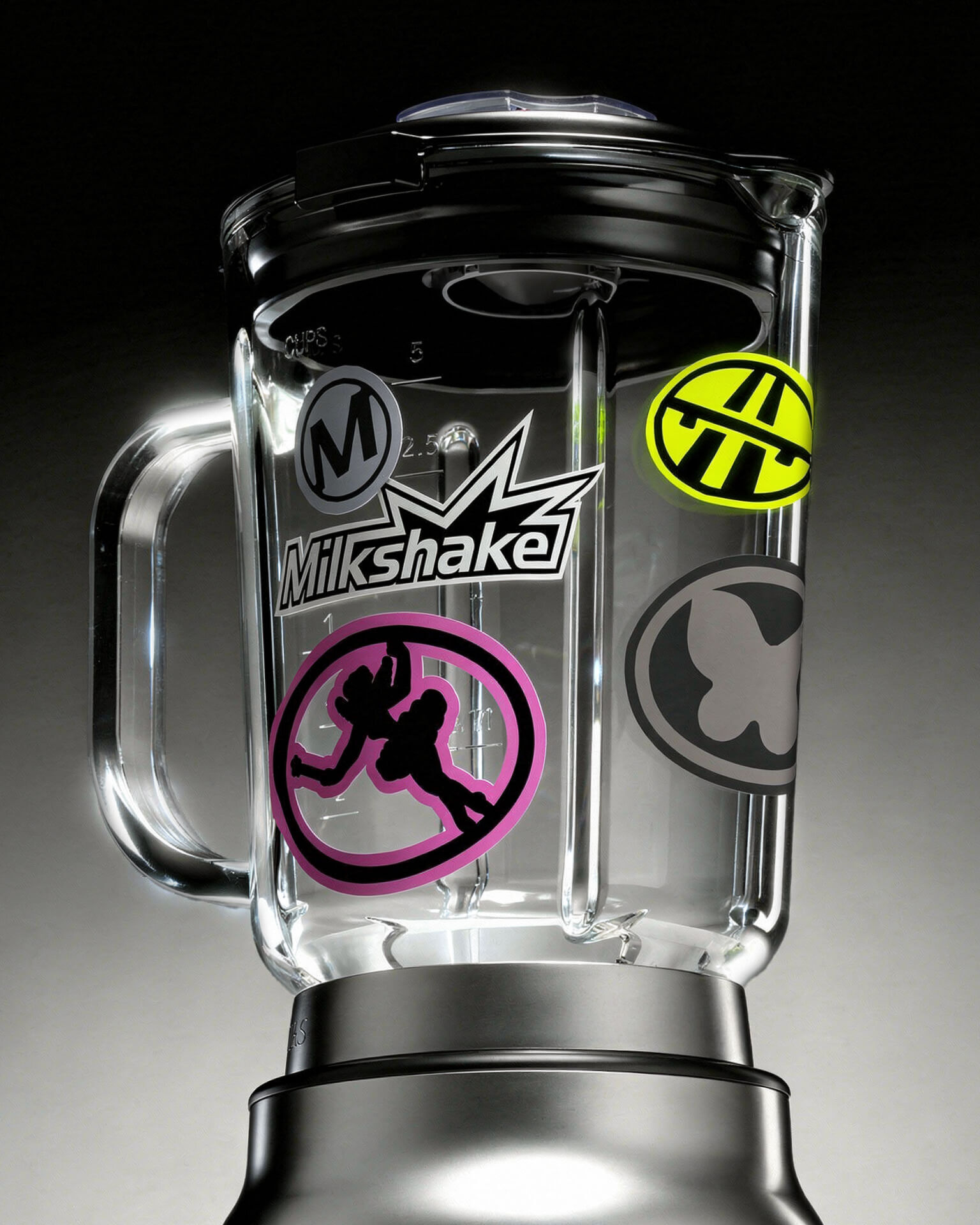 Bol de mixeur transparent couvert d'autocollants : logo Milkshake en blanc, pastilles jaune fluo, rose et grises