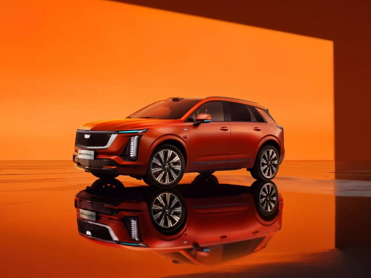Cadillac XT5 PHEV orange, vue de trois quarts avant, posé sur un sol miroir devant un fond orange